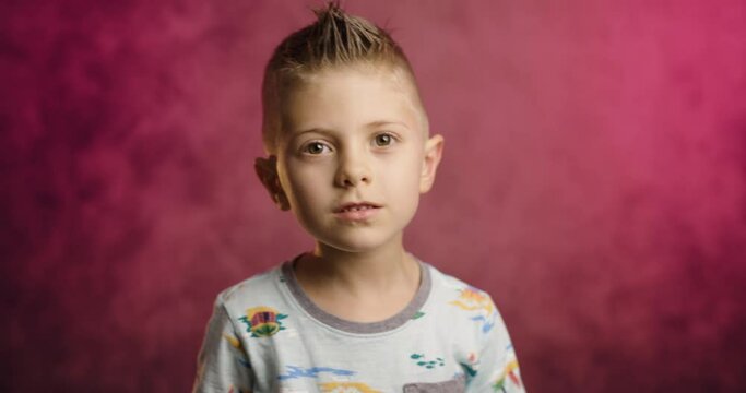 Portrait of excited little boy isolated on a burgundy studio background having fun overjoyed happy little child has fun, kid humor, entertainment concept