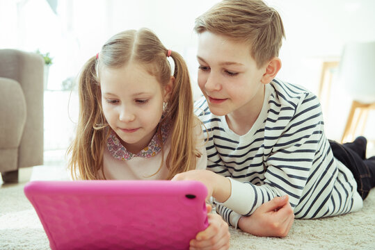 Happy siblings children playing with tablet on floor at home
