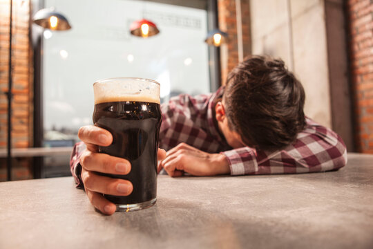 Selective focus on beer glass in the hand of drunk man sleeping at the pub