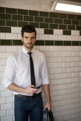 Handsome young man holding mobilephone, standing at underground station.