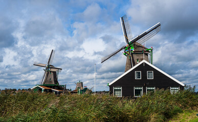 Pair of spinning Dutch windmills and grass blowing in the wind in Zaase Schans, Netherlands