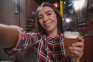 Happy young woman smiling, taking selfie with a glass of beer at the pub