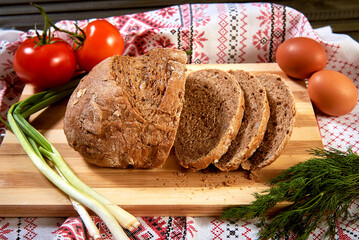 fresh homemade bread on a wooden board on the background of a towel with an embroidered pattern. eggs, tomatoes, greens
