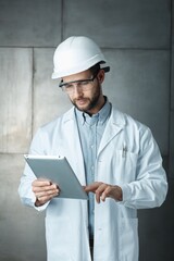 Portrait of confident young engineer wearing protective hardhat using tablet.