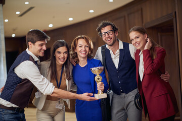 A group of cheerful business people with the trophy won posing for a photo at the hotel hallway....