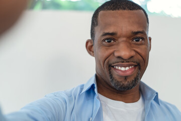 Portrait of African American handsome man smiling friendly aking selfie of himself in their living...