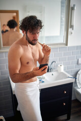 Young handsome man having a call while brushing teeth in the bathroom. Hygiene, bathroom, morning