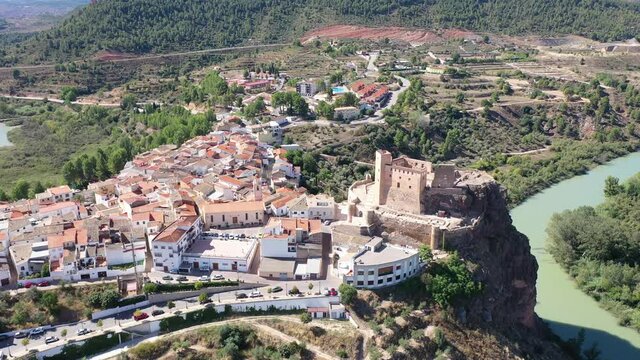 Scenic aerial view of medieval Cofrentes Castle towering over city residential buildings atop rocky cliff over Cabriel River, Valencia, Spain. High quality 4k footage