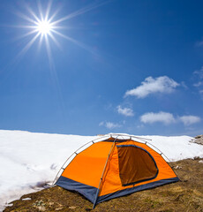 orange tent stay on the hill slope  with  snow under a sparkle sun, travel background