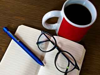 Offenes Notizbuch, Kugelschreiber, Brille zum Lesen und Schreiben, eine Tasse Kaffee auf einem Tisch