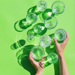 Water glasses on a green background, trendy light and shadow