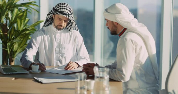 Couple of Adult Muslim Businessmen in White Kandura Clothes Sitting in Modern Office Enterprize Planning Construction of New Company. Cityscape View.