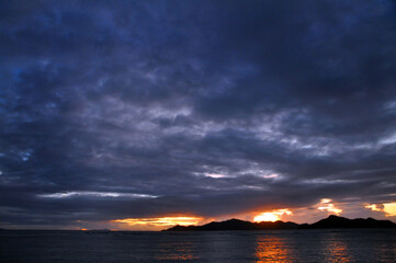 Stunning and colourful sunset with overcast sky over the Indian Ocean with silhouette of an island and reflection on the sea. Seychelles