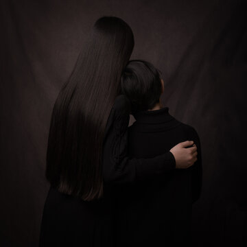 Portrait of sister and brother in black holding each other seen fro back in dark painterly style