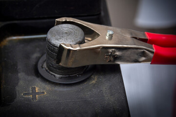Red copper clip attached to the plus terminal. Terminals plus of the old battery. Charging car battery with electric current. Recharging the car battery.