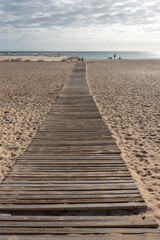 Fototapeta na wymiar Wooden bridge on the sand in selective focus. Wide beach with umbrellas. Morro Jable, Jandia peninsula, Fuerteventura, Canary Islands. 