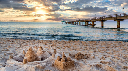 Pier and beach with sand castles in foreground in Zinnowitz at sunset. Baltic Sea, island Usedom, Germany - obrazy, fototapety, plakaty