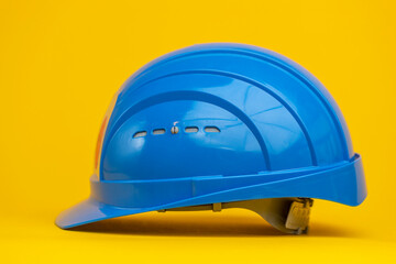 Profile shot of shiny reflecting vibrant blue hardhat on yellow seamless paper background. Studio colorful contrast industrial object concept.