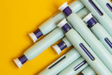 Self applying syringe pens criss cross on seamless yellow background. Studio medical equipment still life concept with auto-injector disposable devices. © Maarten Zeehandelaar