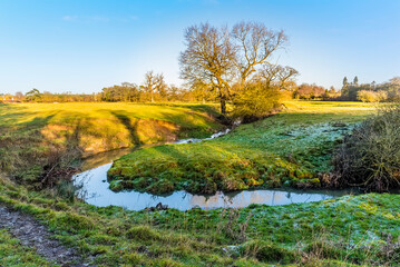 A stream meanders across a meadow near Lubenham, UK on a bright winters day