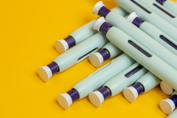 Seamless yellow background with layers of self application syringe pens. Studio medical equipment still life concept with auto-injector disposable devices. © Maarten Zeehandelaar
