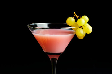 cocktail glass with pink liquid and fresh green grapes with mirrored black background