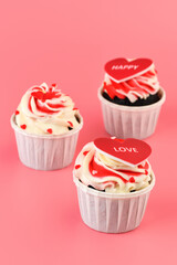 Cupcake. Cupcakes in the shape of a heart in white cups with inscriptions: love,  happy on a pink background. Valentine's Day. Vertical photo