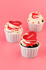 Cupcake. Cupcakes in the shape of a heart in white cups with inscriptions: love,  happy on a pink background. Valentine's Day. Vertical photo