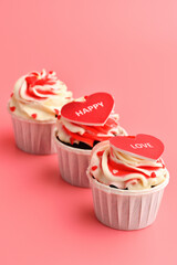Cupcake. Cupcakes in the shape of a heart in white cups with inscriptions: love,  happy on a pink background. Valentine's Day. Vertical photo