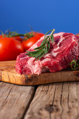Raw pork meat with tomatoes and rosemary on wooden cutting board o blue background. Image for butcher shop. Appetizing view for advertising.