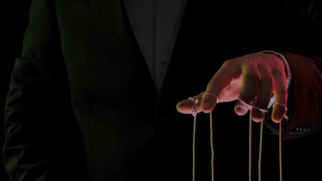 Businessman leader in a suit manipulates the strings of puppets tied to his fingers. Domination, power and submission concept. Close up mans hands illuminated with colored lights. Slow motion.