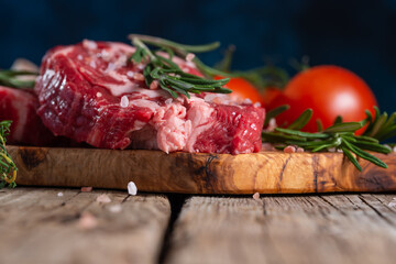 Close-up of raw pork or beef meat with tomatoes and rosemary on wooden cutting board o blue background. Image for butcher shop. Appetizing view for advertising.