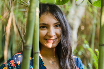 Portrait of young Hispanic woman in the middle of a bamboo forest at sunset - Young woman smiling in the middle of nature in a natural park