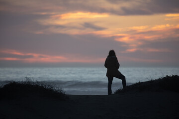 silhouette of a woman alone on a hill at the beach looking at ocean during sunset