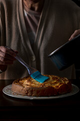 A woman painting gelatin on an apple pie. Unrecognizable person.