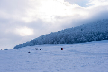 Wintersportler, Schneeschuhwanderer und Spaziergänger laufen durch eine sehr verschneite Landschaft in der Abenddämmerung