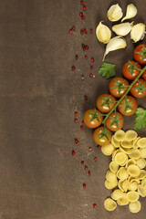 food frame with Italian pasta ingredients. garlic, peppercorns, salt, pasta, cherry tomato, parsley with space for text on wood background.