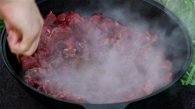cooking process of an oriental dish. red meat boils and stews in oil in a large pot. large traditional Asian cauldron on an open fire, called a Kazan