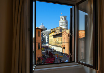 View through an open window of tourists and cafes on the Via Santa Maria, the busy tourist street leading to the Leaning tower in the Tuscan city of Pisa, Italy