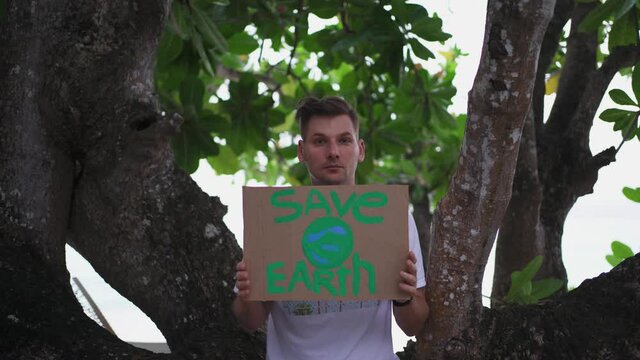 A young man with a sign "Save the Earth" is a caring activist who cares about the environment, pressing social problems of the present time in the massive pollution of the planet with plastic.