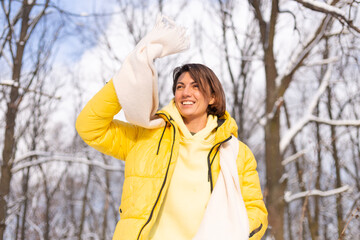 Beautiful young cheerful woman in a snowy landscape winter forest having fun rejoices in winter and snow in warm clothes, scarf