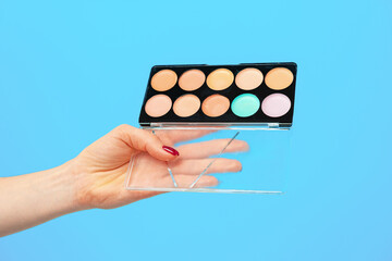 Female hand holding cosmetic palette against blue background