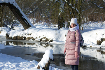 Woman in winter clothes on a walk in the park. A river flows nearby. There is a lot of snow around.