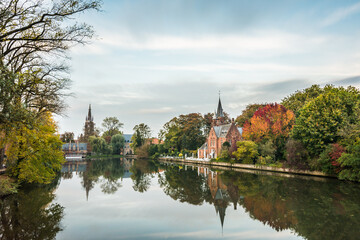 Fototapeta na wymiar Autumn mood by the Minnewater (Lake of love) in Bruges. Bruggy Belgium Minnewater. A historic church by the water.
