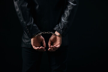 Close up of male prisoner with handcuffs over black background. Arrested man because of illegal action. Focus on hands.