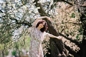 Young attractive woman with curly long hair posing in spring blooming garden, apple trees