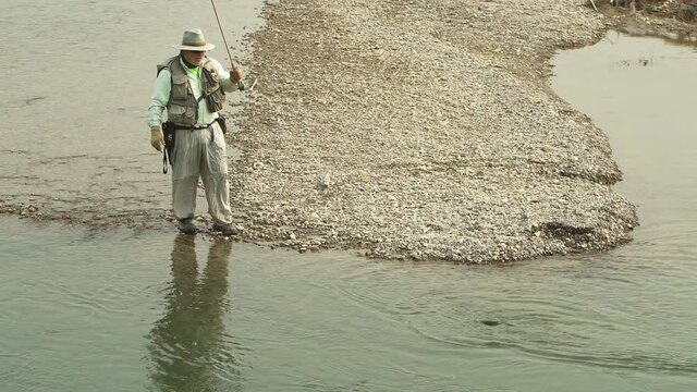 Fisherman lets the hooked fish tire itself out as it splashes in the Buffalo Fork River, Bridger-Teton National Forest, Wyoming. Static shot.