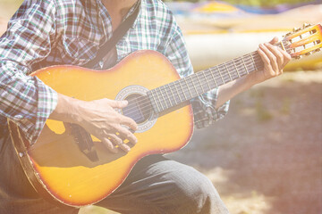 An unrecognizable male musician dressed in a casual style is holding an acoustic wood guitar in...