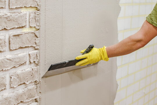 Plasterer smoothing  plaster  on wall for making texture of torn brick made of cement plaster by hand. Tape under plaster on wall to imitate decorative brick. home repair