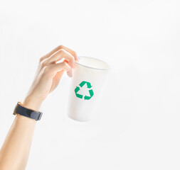Person’s hand hold up an empty takeaway paper cup with green recycle symbol on white background. Concept idea of care, responsible, recycling and save the environment and globe from global warming.